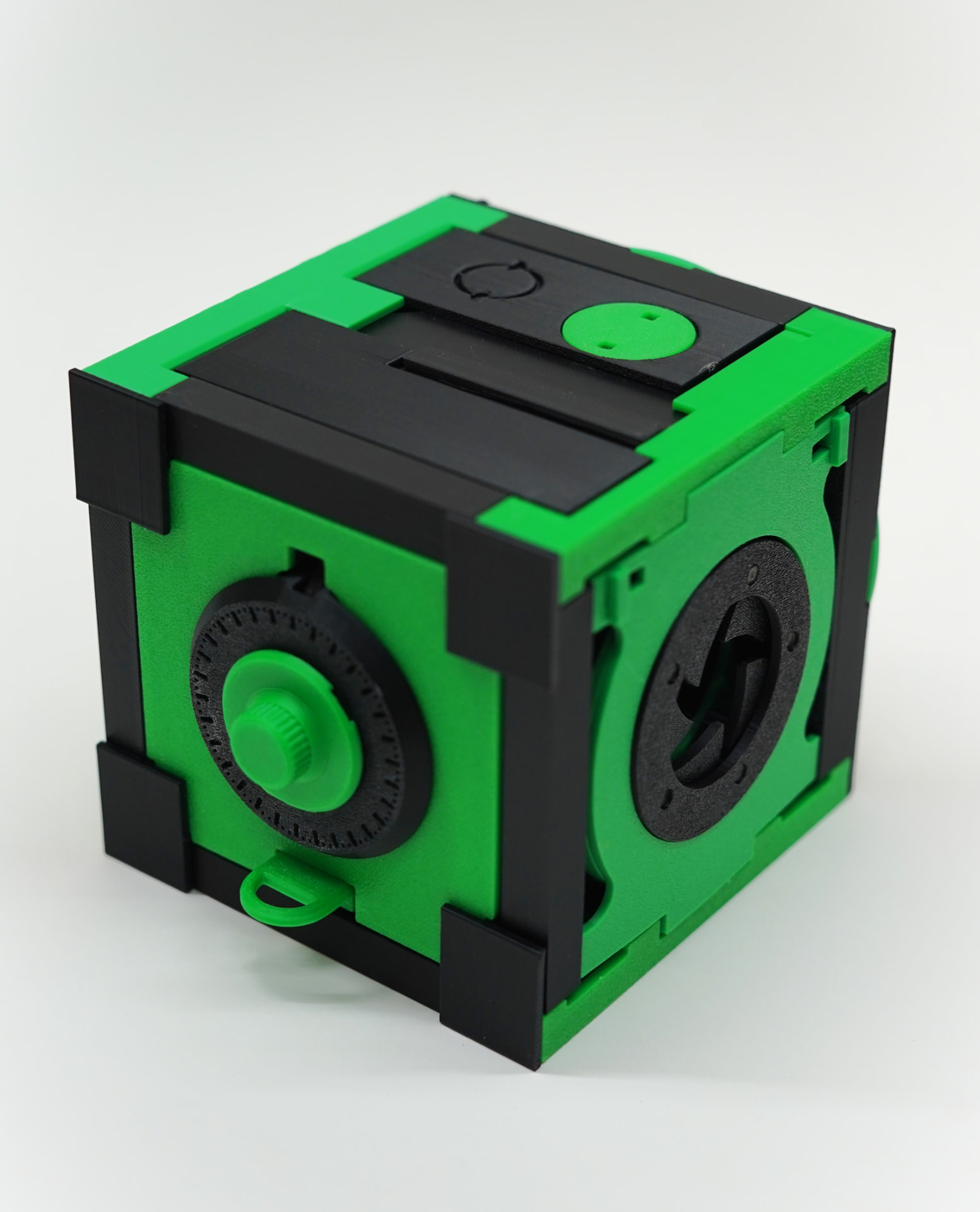 The Cube, a green and black mechanical puzzle box with a rotary dial and an iris mechanism, on a white studio background